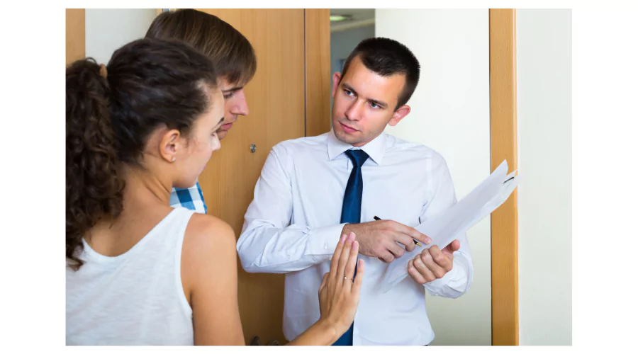 A CCS representative in a shirt and tie holding documents while discussing with a couple at their doorstep, capturing a typical consultation scenario at CCS Offices.