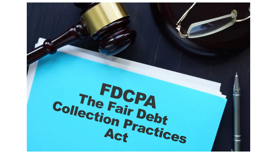 A close-up of a blue folder labeled 'FDCPA The Fair Debt Collection Practices Act' resting on a dark table, with a judge's gavel and eyeglasses placed beside it, and a black pen in the foreground. This represents the legal documentation and authority concerning debt collection laws.
