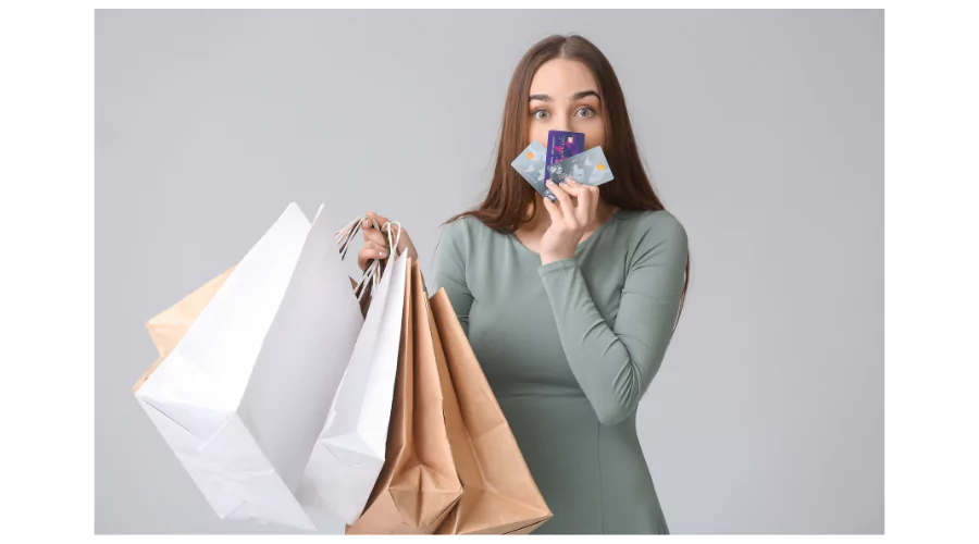 A woman holding shopping bags and a credit card to her mouth with a surprised expression, representing the pitfalls of 'overspending'.