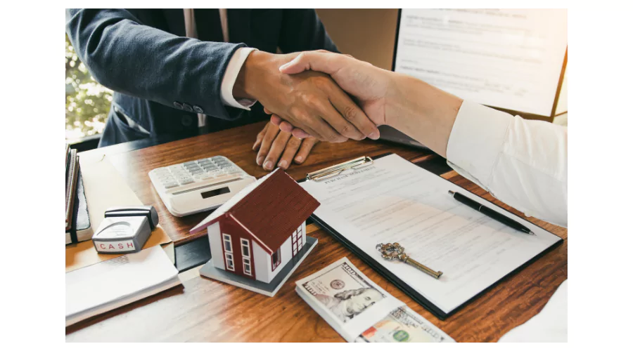 Handshake over home mortgage documents with property deed and house key, illustrating the completion of a real estate transaction.
