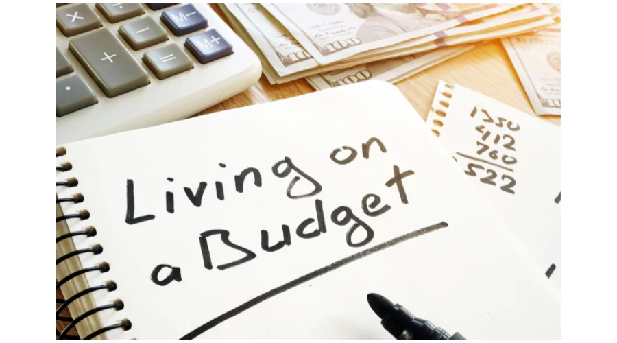 A notebook with 'Living on a Budget' handwritten on the page, next to a calculator and some cash, with notes of financial calculations visible. This setup suggests planning and managing personal finances for a sustainable lifestyle.