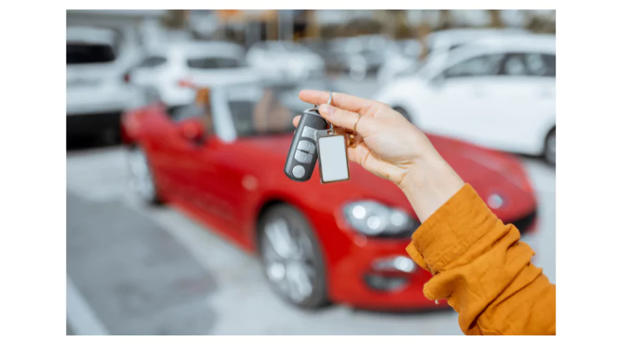 Hand holding car keys with a red sports car in the background, symbolizing new car purchase or auto loan approval.