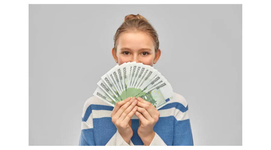 A young teenager holding a fan of 100 euro bills over her face, conveys the concept of financial independence which can be achieved through jobs for 15-year-olds.